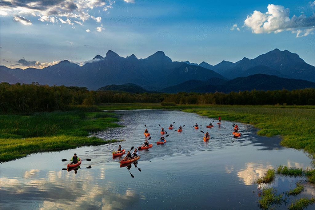 Foto aéra de várias pessoas andando por canais que serpenteiam a mata atlântica, o céu azul refletido na água e as montanhas da serra do ibitiraqueiri ao fundo.